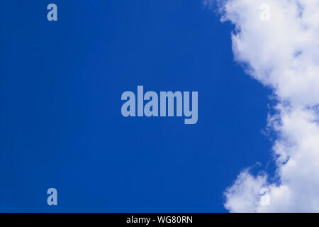 A clear blue sky with clouds on the right side. The clouds are loose and white. The left side is therefore empty. Stock Photo