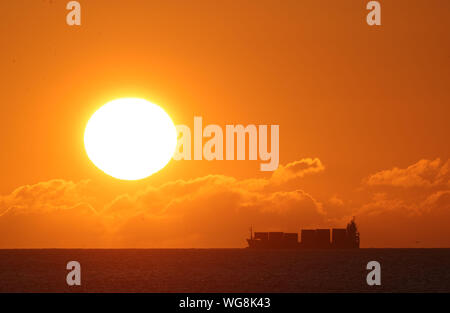A cargo ship on the horizon as the sun rises at Seahouses on the North Northumberland coast. Stock Photo