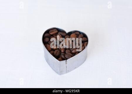 Closeup of roasted beans at heart  shape at light wooden background/ Raw coffee beans Stock Photo