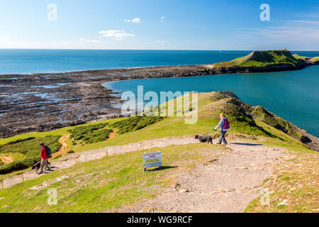 Dog walkers at the end of the Gower peninsula with Worms Head beyond South Wales, UK Stock Photo