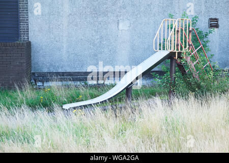 Play park derelict abandoned slide in overgrown grass at playground Stock Photo