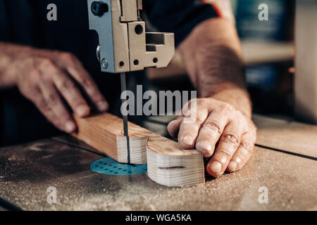 Carpenter working in workshop. Joiner labourer cuts wooden plank on jigsaw machine. Handwork, carpentry concept, woodworking. Stock Photo