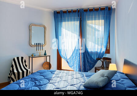 Elegant bedroom decorated in a classic minimal style, with the sunlight coming in from the big window creating an intimate mood Stock Photo