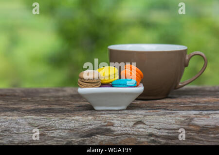 Cup of coffee and Colorful Macaroons in dish on wooden table in garden Stock Photo