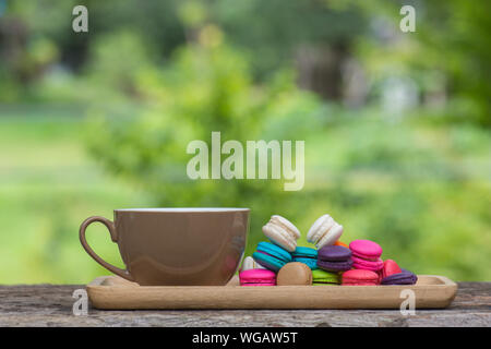 Cup of coffee and Colorful Macaroons in dish on wooden table in garden Stock Photo