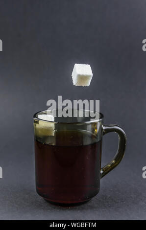 Sugar cubes fall into black tea on a black background. Stock Photo