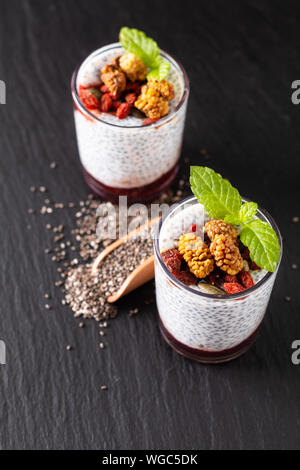 Healthy food concept Chia seeds, milk pudding with goji, white mulberry and mix dried seeds in small Glass on black slate board background Stock Photo