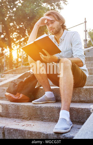 Student read a book sitting on the stairs in campus. Shot with sunflare Stock Photo