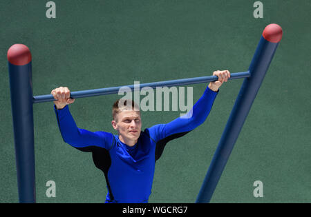 Shot of strong athlete man doing pull-up on horizontal bar over the grass background. Stock Photo