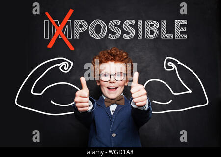 Young boy student with text possible holding thumbs up on blackboard background. Success and develop concept Stock Photo