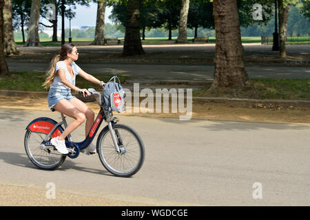 Young woman riding Santander hired bicycle in Hyde Park, London, United Kingdom Stock Photo