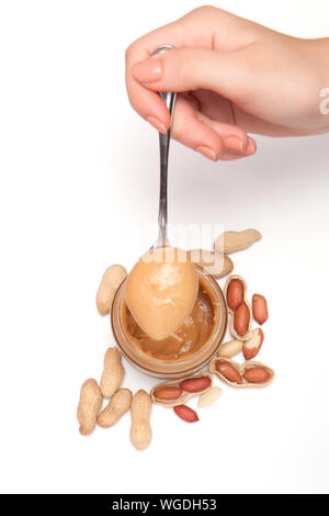 Creamy peanut butter in glass jar, peanut and spoon isolated on white background. A traditional product of American cuisine Stock Photo