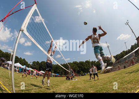 A man jumps high to spike the ball in a triples grass volleyball tournament, featuring three-person teams, on August 25, 2019 in Doraville, GA. Stock Photo