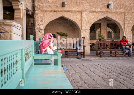 Doha, Qatar - 3 dec 2016: Two women from the Philippines and two Indian men are sitting on town on turquoise benches in Souq Wakif, Doha Stock Photo
