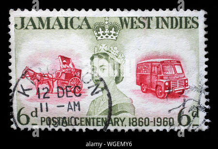 Stamp printed in Jamaica shows and Queen Elizabeth II and coach and bus, the 100th Anniversary of Jamaican Postal Service, circa 1960. Stock Photo