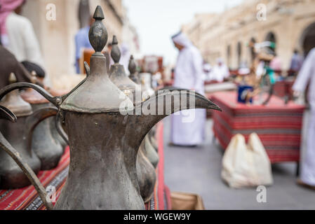 Doha, Qatar - 25 Nov 2016: A traditional Arabic coffee jug and men wearing Gulf traditional clothing in a blurred background. Taken in Souq Wakif, Doh Stock Photo