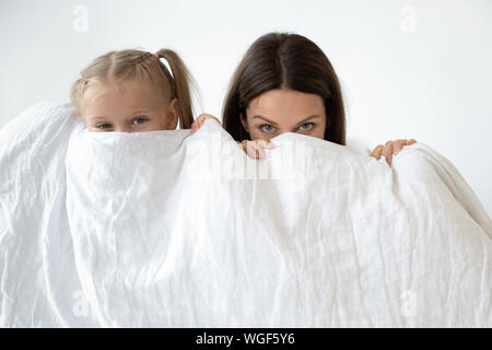 Mother and daughter hiding behind white blanket indoors Stock Photo