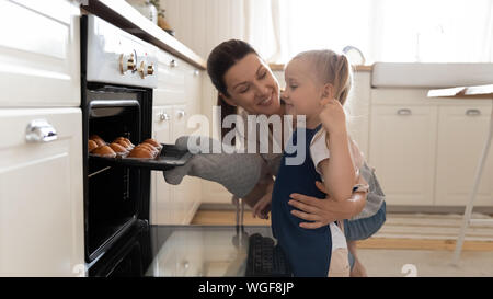 Little girl and beautiful mother taking muffins out the oven Stock Photo