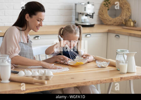 Little girl and mother cooks pie together in kitchen