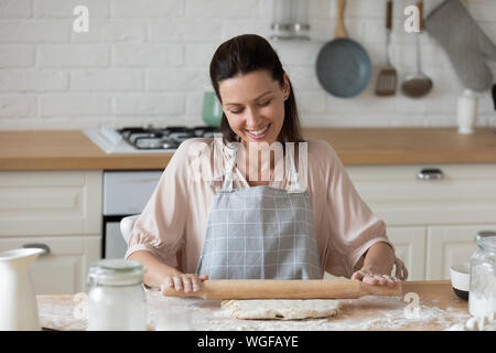 Woman flattening dough with rolling pin in the kitchen Stock Photo