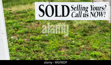 A white sold sign with black letters hanging over grass with room for copy space underneath. Stock Photo