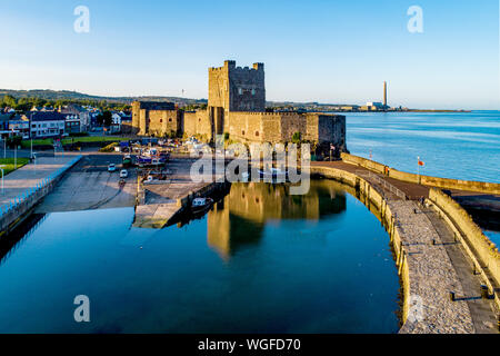 Medieval Norman Castle and harbor with boat ramp and wave breaker in Carrickfergus near Belfast, Northern Ireland, UK. Aerial view  in sunset light.