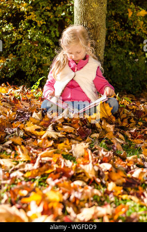 little girl sittig by the tree trunk with book in hand Stock Photo
