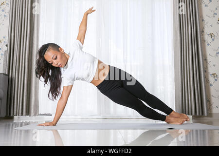 Attractive young asian woman exercising and sitting in yoga position while resting at home