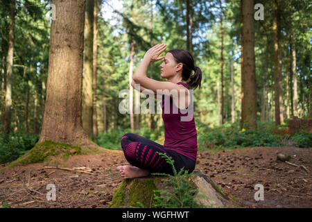 woman sitting on a tree stump in a forest meditating, practicing yoga. Stock Photo