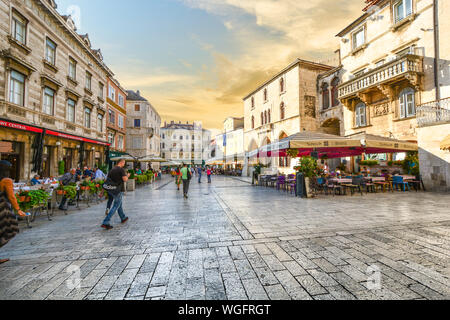 Tourists enjoy the morning in Old Town Split Croatia as they walk through People's Square with outdoor sidewalk cafes and the ancient buildings Stock Photo