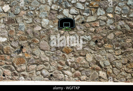 A basketball backboard, rim and net under midday sun, mounted on masonry wall outdoors. Stock Photo