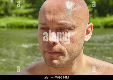 Bald man of mature age with a moth on the tip of his nose, against the background of a river in the wild, ecotourism. Stock Photo