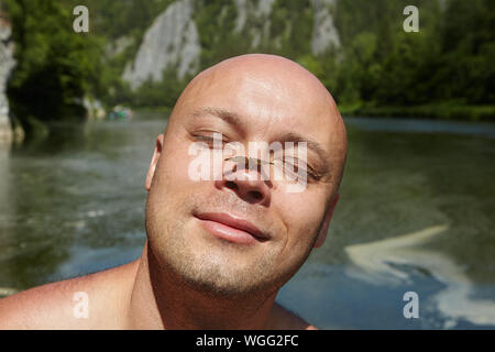 Ecotourism in the ecosystem of a forest river, a bald man closed his eyes and set his face to the sun, a small brown butterfly sits on his nose. Stock Photo