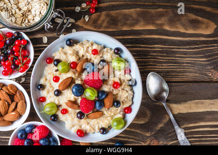 oatmeal porridge with fresh berries and nuts in a bowl on rustic wooden background for healthy diet breakfast. top view with copy space Stock Photo