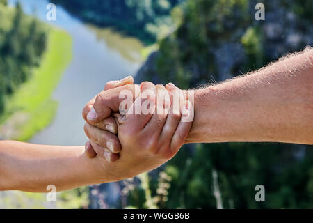 The male hand embraces the female hand against the backdrop of the natural landscape. A helping hand extended by a man to a woman on a hiking trip. Mu Stock Photo