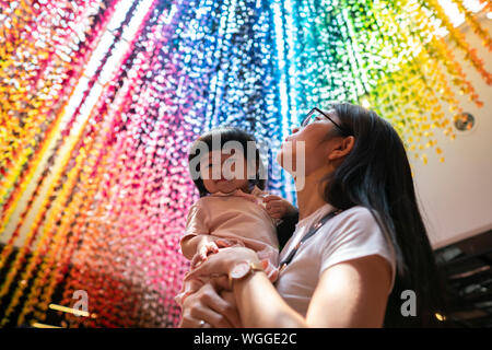 Young asian mother holding her girl overlooking on rainbow paper cranes. Stock Photo