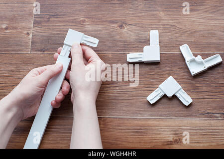 Accessories for plastic windows. Plastic area for mosquito nets and aluminum profile in the hands. On a brown wooden background. Stock Photo