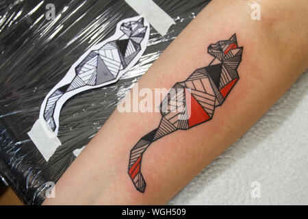 Kharkiv, Ukraine - June 4, 2017: Close-up fresh tattoo on client's arm next to a tattoo sketch, reddened skin from tattoo machine work Stock Photo