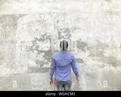 Backside of young man in checkered blue shirt and sunglasses standing against concrete gray wall. looking at background empty copyspace. Stock Photo