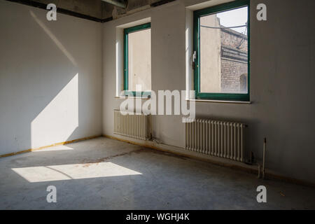 Interior view of empty abandon room with radiator heaters, glass windows and air duct system on ceiling. Stock Photo