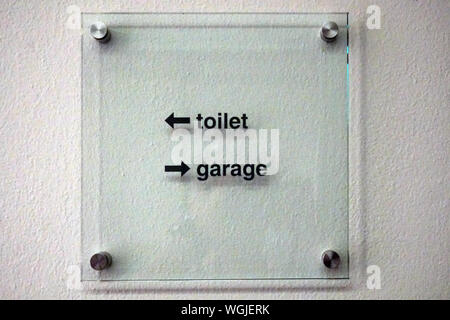 The toilet-garage sign with two arrows in the square plexiglass hanged on the white wall Stock Photo