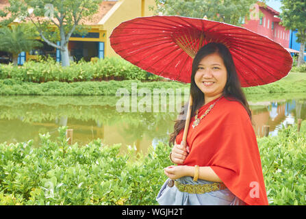 Portrait Of Smiling Young Woman Standing With Red Umbrella By Pond