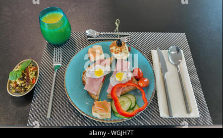 Breakfast with ham sandwiches, smoked salmon, bread, vegetables, bulgur rice salad and orange juice served in small family hotel on tablecloth closeup Stock Photo