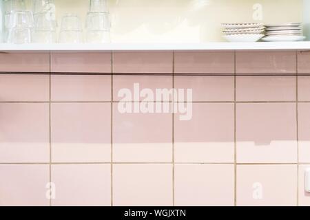 Glasses And Plates On Shelf Over Tiled Wall In Kitchen