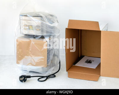 Drip-type coffee maker is in cellophane and near its cardboard box with instruction manual. Unpacking a new coffee machine. Home electrical appliances Stock Photo