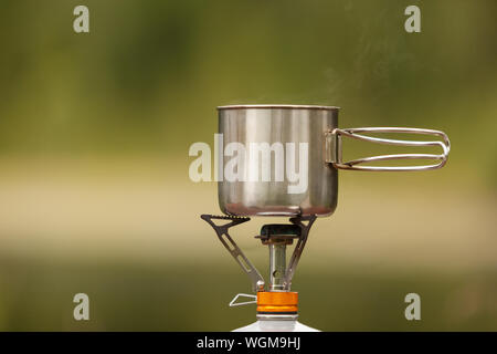 The camping iron mug with a gas burner on natural bokeh background Stock Photo