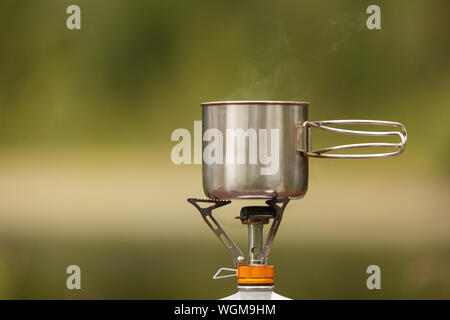 The camping iron mug with a gas burner on natural bokeh background Stock Photo