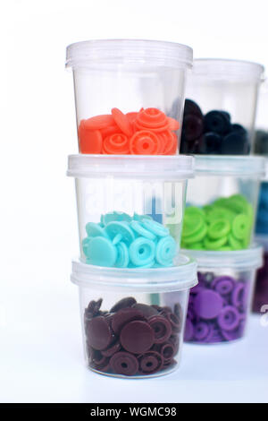 Staples of colorful plastic snap fastener buttons in transparent containers on white background Stock Photo