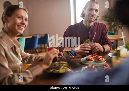Group of friends enjoying lunch together sitting at table in cafe, focus on handsome young man, copy space Stock Photo