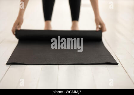 Woman practicing yoga, rolling black mat on floor close up Stock Photo